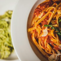 a plate of pasta with sauce and spinach on the side